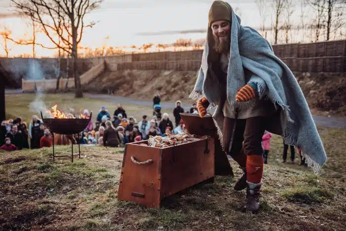 Levendegjøring av vikingtiden. En mann i tidsriktige klær poserer for kamera. I bakgrunnen sitter publikum.